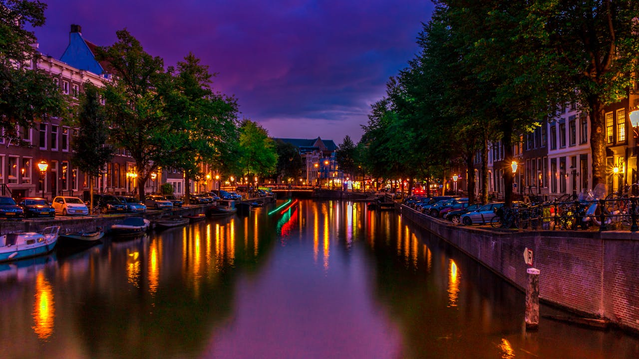 A vibrant night scene of Amsterdam's canal with colorful reflections and city lights.