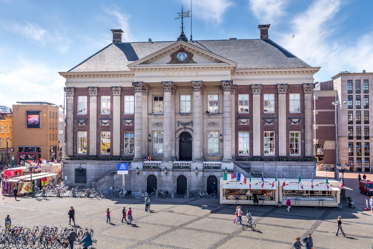 Groningen City Hall facade with bustling market stalls and cyclists on a sunny day.